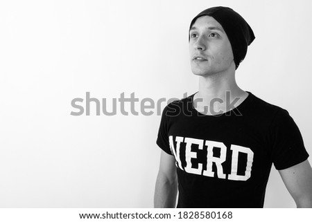 Studio shot of young handsome nerd man thinking and looking up while wearing hat against white background