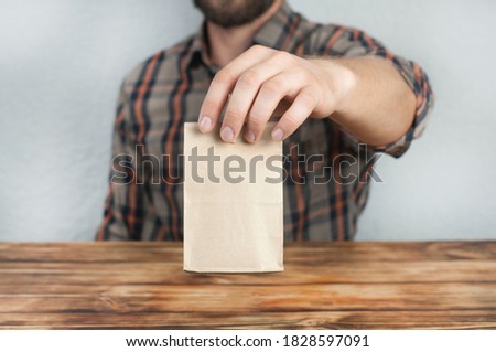 A young man holds a paper bag in his hand. Present. Sitting at a wooden table