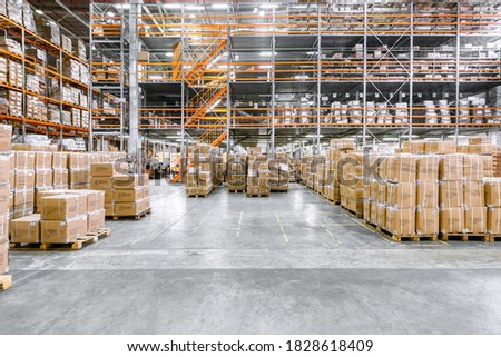 Large industrial warehouse. Tall racks are completely filled with boxes and containers. Many cardboard boxes stand on a loading dock. Royalty-Free Stock Photo #1828618409