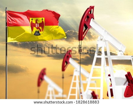 Oil rigs against the backdrop of the colorful sky and a flagpole with the flag of Burgenland. The concept of oil production, minerals, development of new deposits.