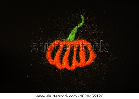 Pumpkin layout for Halloween on a black background with orange sequins. Decorative composition for a holiday. The view from the top. Orange pumpkin with a green tail. Copy space
