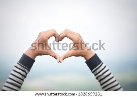Heart-shape hand gesture on green valley background with selective focus