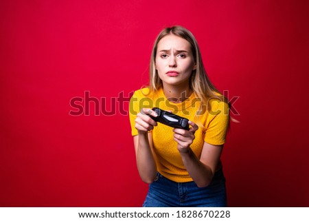 Young blonde gamer woman using gamepad playing video games isolated over red background