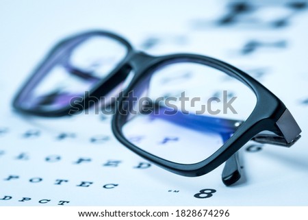 Modern reading glasses on a eye sight test chart. Blue toned image.