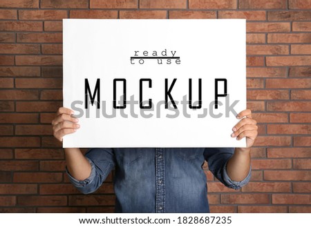 Man holding white poster with text Mockup Ready To Use near brick wall