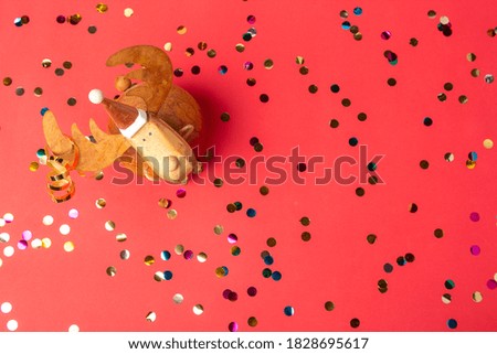Christmas bauble deer and colorful shiny confetti  on red background. Happy New Year celebration. Flat lay, top view