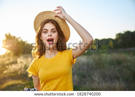 Cheerful woman with open mouth holds hand on hat nature vacation photographer