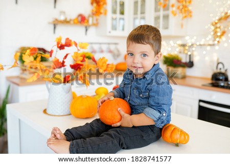 cute child little boy sitting on the table in kitchen at home with autumn decorations