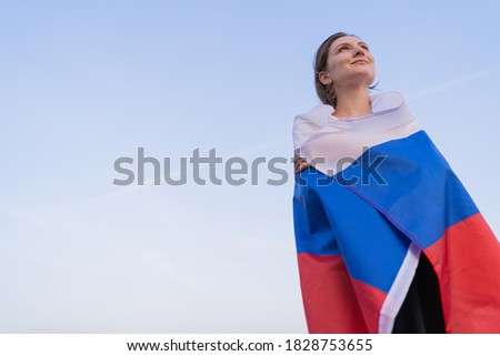 Patriot woman. A beautiful Russian woman with the flag of the Russian Federation looks to the future against the bright sky at sunset. A place for your text