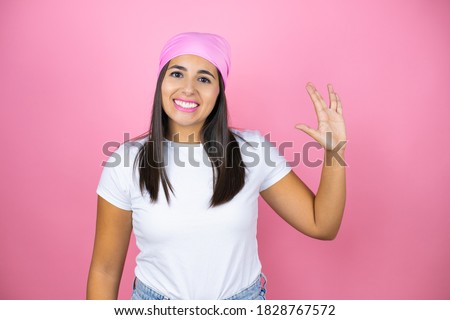 Young beautiful woman wearing pink headscarf over isolated pink background doing hand symbol