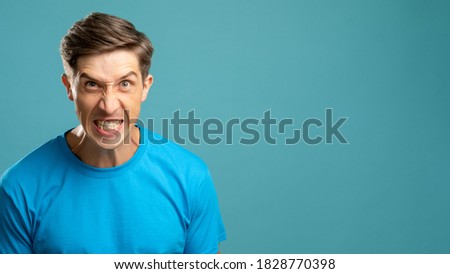 Furious male portrait. Annoyed mad. Abusing pressure. Aggressive emotion. Psychology therapy. Angry uncontrolled young man looking at camera isolated on blue copy space. Royalty-Free Stock Photo #1828770398