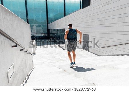 fitness, sport, training and lifestyle concept - young man in headphones running downstairs outdoors