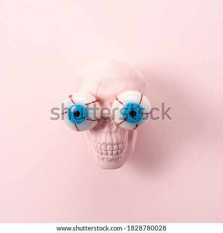 Pink skull with eyeballs on pink background. Minimal holiday fun spooky concept.