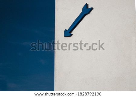 blue arrow on white wall and blue sky