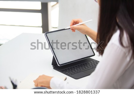 
Cropped shot of Business women are using a tablet showing a white screen to put your text and pictures with a pen working on a table beside the window.