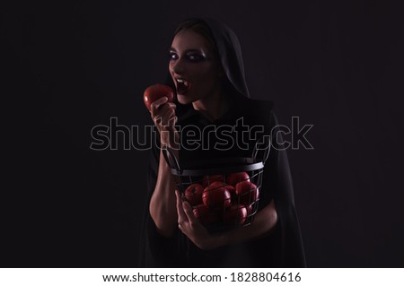 Mysterious witch eating apple on black background