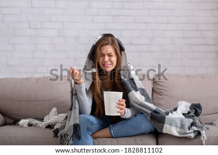 Heartbroken young woman eating ice cream from bucket while watching romantic movie on TV at home. Sad lady crying over breakup or relationship problems, feeling depressed and lonely Royalty-Free Stock Photo #1828811102