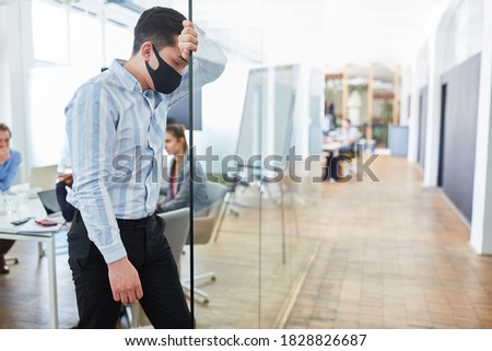 Exhausted young businessman in the office with face mask because of Covid-19 Royalty-Free Stock Photo #1828826687