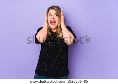 Young caucasian woman isolated on purple background covering ears with hands trying not to hear too loud sound.