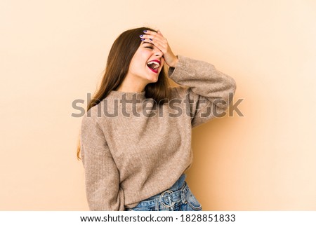 Young caucasian woman isolated en beige background laughs joyfully keeping hands on head. Happiness concept.