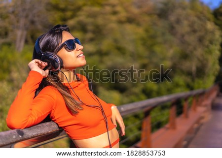 Lifestyle, brunette Caucasian girl enjoying music with headphones in a park. Young girl in red t-shirt and jeans, copy space and paste