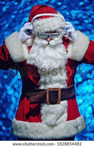 DJ Santa Claus in glasses covered with snow and headphones. Christmas songs and music. Disco lights in the background. 