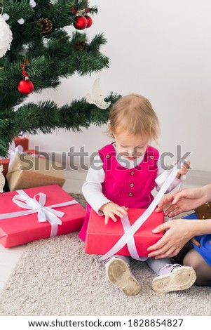 Smiling mother open Christmas presents with baby daughter in room at background. Winter season. Motherhood. Merry Christmas. New Year.