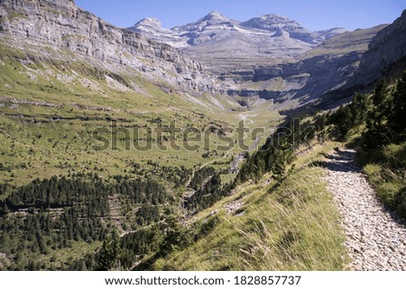 High mountain landscape in summer with the Ordesa valley in the background with the trekking path that leads to the mountain peaks. In the heart of the Pyrenees. Panoramic view in horizontal.
