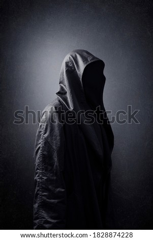 Scary figure in hooded cloak in the dark. Royalty-Free Stock Photo #1828874228