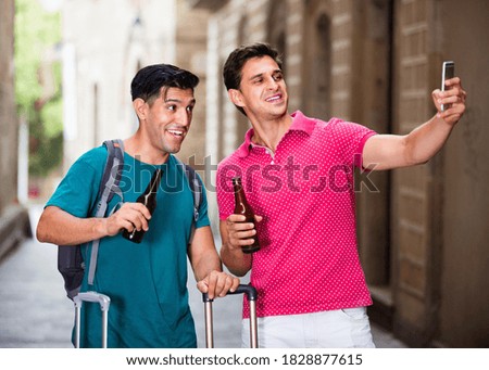 Happy cheerful smiling men tourists with beer are making selfie in unknown city.