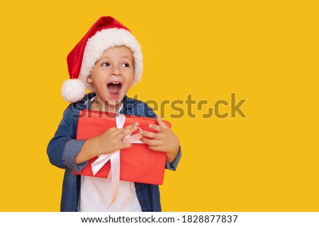 Portrait of a satisfied little child boy in christmas Santa hat. laughing isolated over yellow background. Holds a gift box. Preparing for the New Year holidays Royalty-Free Stock Photo #1828877837