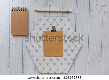 brown blank piece of papaer on octagon shaped note board beige pencil and brown notebook white wooden background. Bee pattern note board. Stationery scene.
