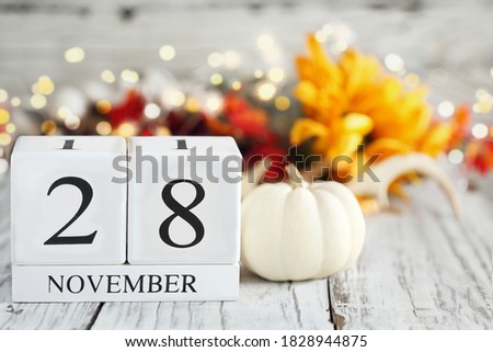 Cyber Monday. White wood calendar blocks with the date November 28th and autumn decorations over a wooden table. Selective focus with blurred background. 