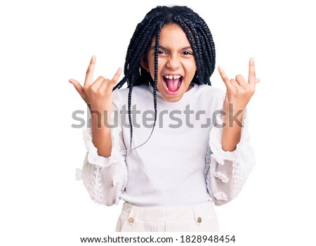 Cute african american girl wearing casual white tshirt shouting with crazy expression doing rock symbol with hands up. music star. heavy concept. 