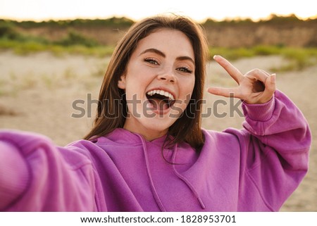 Young caucasian beautiful woman gesturing peace sign and taking selfie photo outdoors