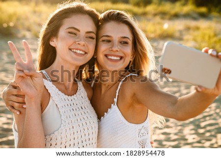 Two young caucasian happy women smiling and taking selfie photo at cellphone while walking outdoors