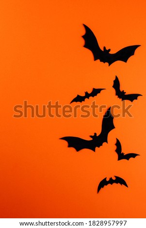 Group of different large and small silhouettes of flying black bats on bright orange vertical paper background. Silhouettes are hand carved from cardboard. Flat lay with Halloween symbols. Copy space.
