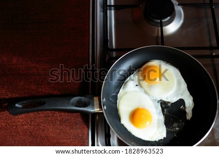 making english breakfast. cooking scrambled eggs. two broken eggs in a frying pan on the stove. two eggs are fried in a pan. view from above. stove, table and frying pan. kitchen utensils.