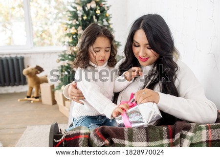 Beautiful young mixed race family: mom and little daughter getting ready for christmas and opening presents near the christmas tree
