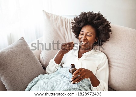 Sick woman sitting at the window of the house and drink the bitter medicine. Girl drinks a medicine. She is being treated for a cough. Treatment of influenza. Ill woman  taking cough syrup