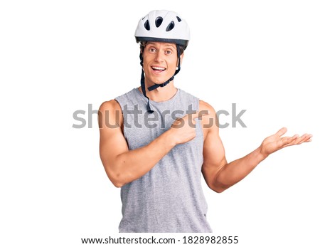 Young handsome man wearing bike helmet amazed and smiling to the camera while presenting with hand and pointing with finger. 