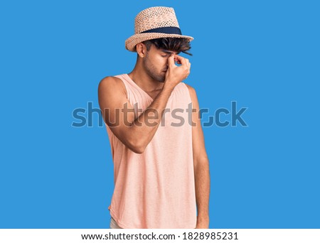 Young hispanic man wearing summer hat tired rubbing nose and eyes feeling fatigue and headache. stress and frustration concept. 