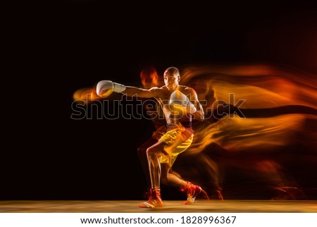Speed. Professional boxer training isolated on black studio background in mixed light. Man in gloves practicing in kicking and punching. Healthy lifestyle, sport, workout, motion and action concept. Royalty-Free Stock Photo #1828996367