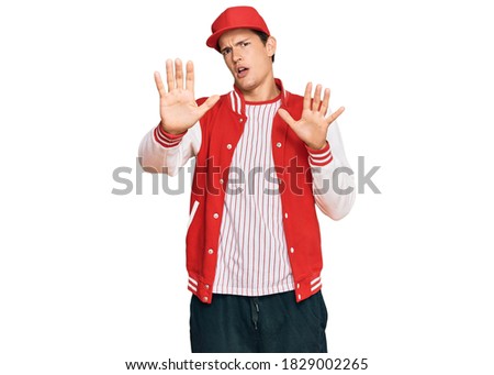 Handsome caucasian man wearing baseball uniform afraid and terrified with fear expression stop gesture with hands, shouting in shock. panic concept. 