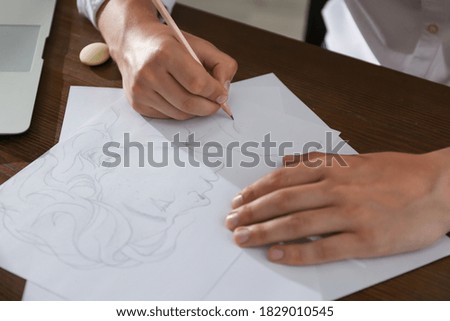 Man drawing portrait with pencil on sheet of paper at wooden table, closeup