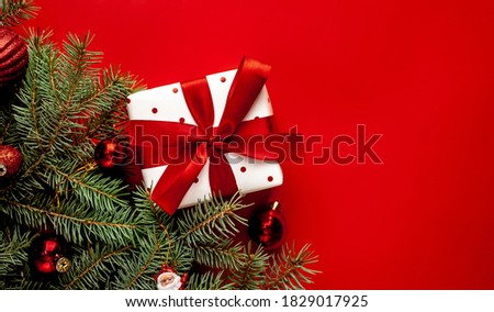 Christmas composition on a red background with a white gift box, with a red ribbon with fir branches, toys, copy space for your congratulations