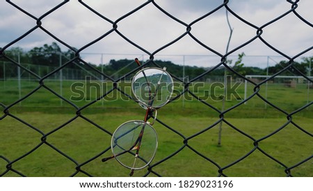 Artistic photography, moment of calm and reflection: glasses hanging on the grid of a football field