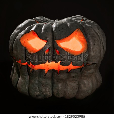 Grey jack o lantern with black background and scary face lit with a candle.