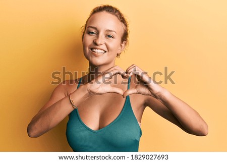 Beautiful caucasian woman wearing sleeveless shirt over yellow background smiling in love showing heart symbol and shape with hands. romantic concept. 