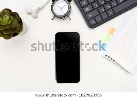 top view of a phone with a screen mockup, a coffee cup of writing supplies, a pens, a notepad on a white wooden table background. Top view of the work area, copy space